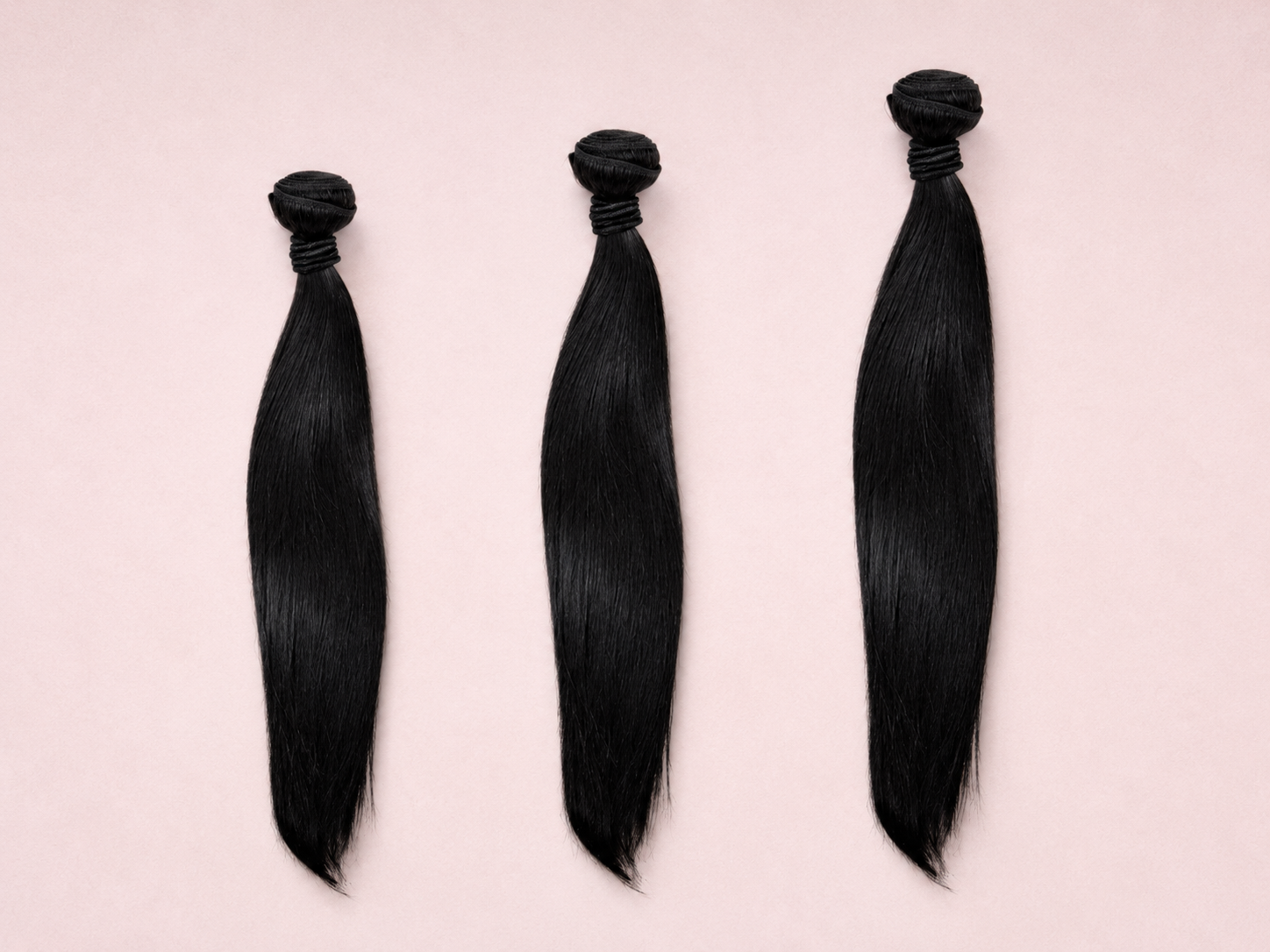 Three bundles of black hair extensions on a light pink background